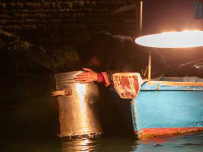 ...e, sporgendosi leggermente dalla barca, regge con entrambe le mani il contenitore cilindrico in metallo. Il fondo in vetro � immerso in acqua e gli serve per scorgere eventuali banchi di pesci
